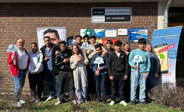 Gruppenfoto an der Schule an der Deilich unter dem Schild „Schule ohne Rassismus – Schule mit Courage“